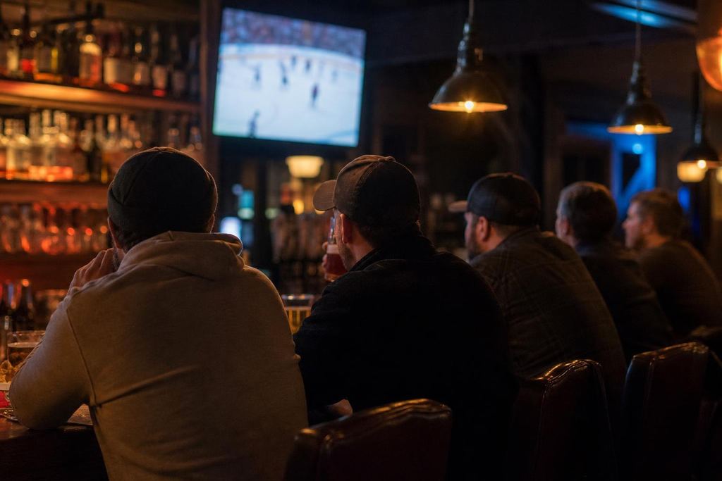 Friends sharing nachos at a dim pub bar late at night, a single TV glowing (AI-generated image)