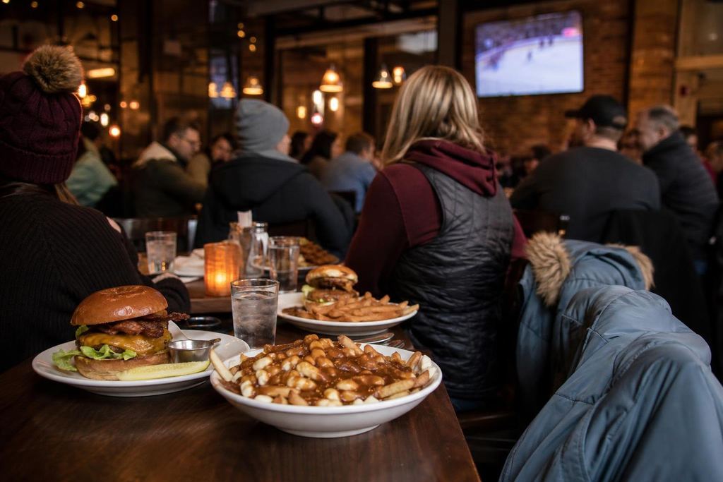 Burgers and poutine on a restaurant table, winter coats hung on chair backs before a game (AI-generated image)
