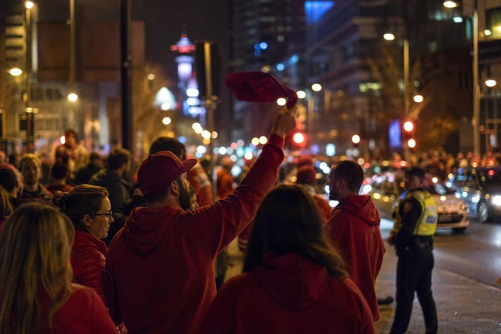 Crowd of hockey fans in red celebrating on a city sidewalk at night after a win (AI-generated image)