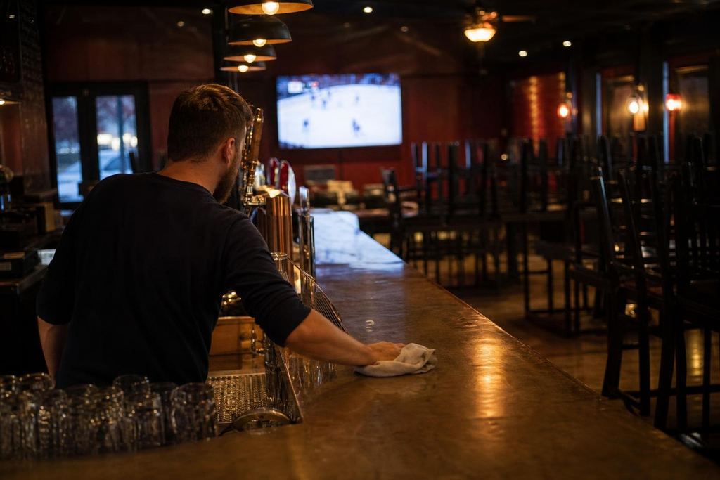Chairs stacked upside down on tables in an empty sports bar, one TV still on (AI-generated image)